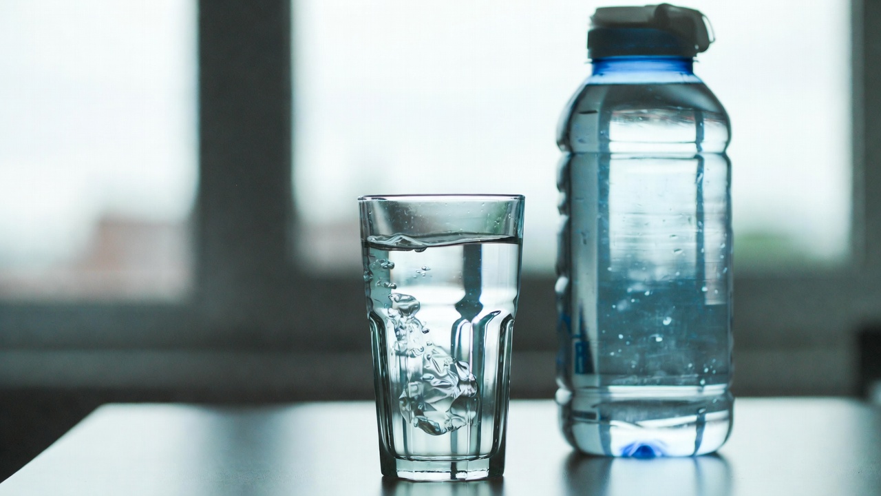 Bicchiere d'acqua accanto a una bottiglia, a illustrare l'importanza di distribuire i liquidi nella giornata