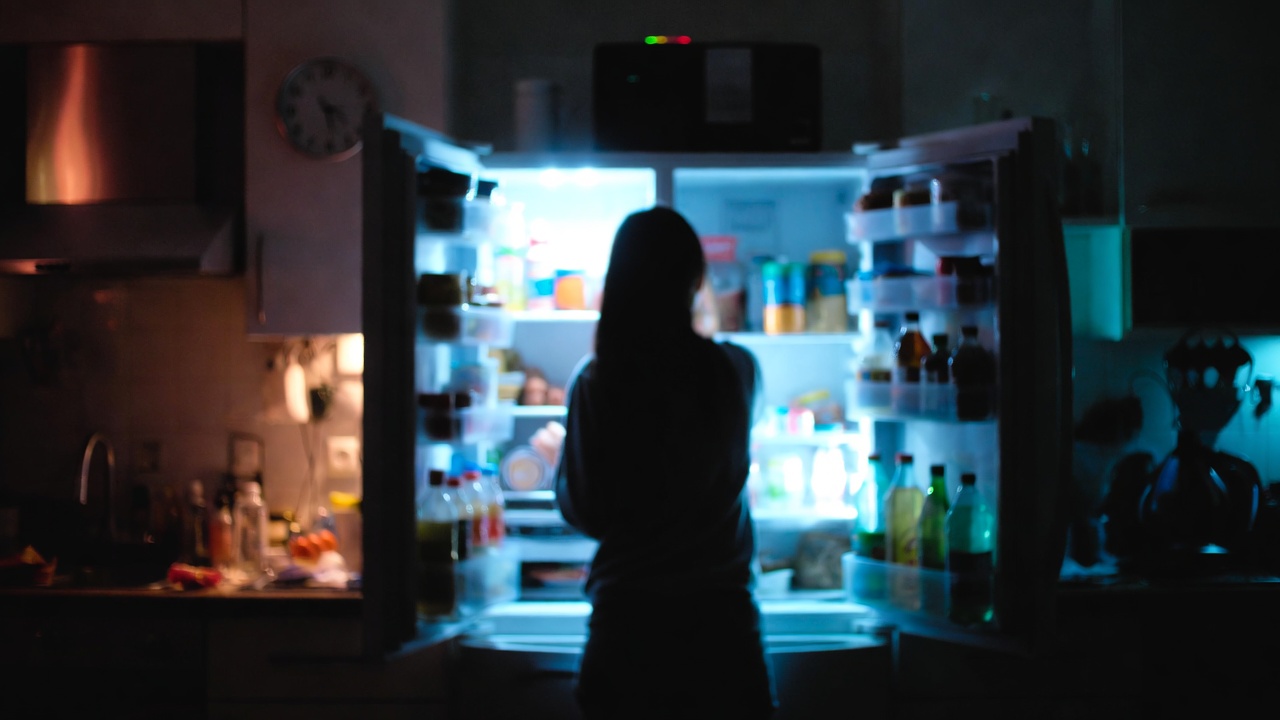Persona di spalle davanti al frigorifero aperto di notte, per l’articolo sulla fame nervosa serale