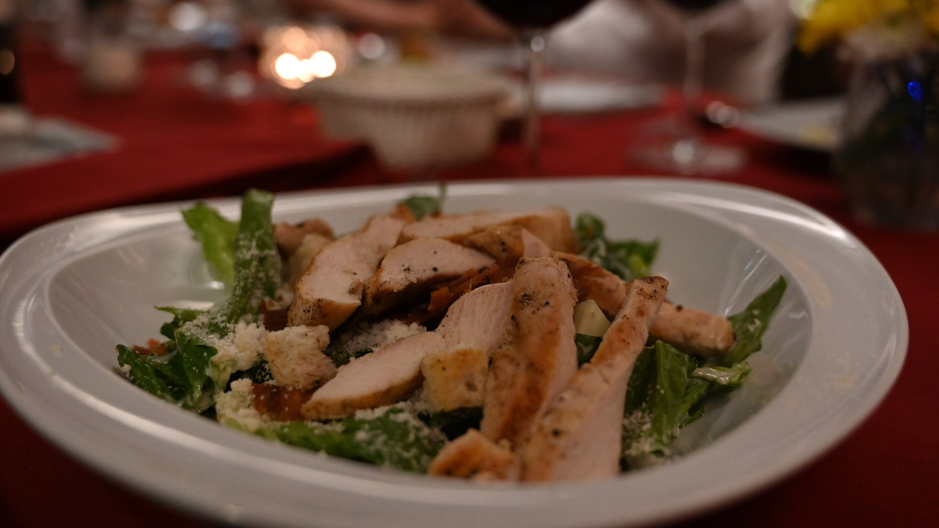 Piatto con insalata e pollo grigliato servito su una tavola serale illuminata da candele: cosa succede a glicemia, ormoni e sonno quando si cena tardi la sera