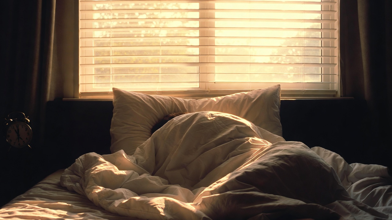 Camera da letto con sveglia che segna quasi mezzogiorno e luce del sole che entra dalla finestra, la domenica mattina